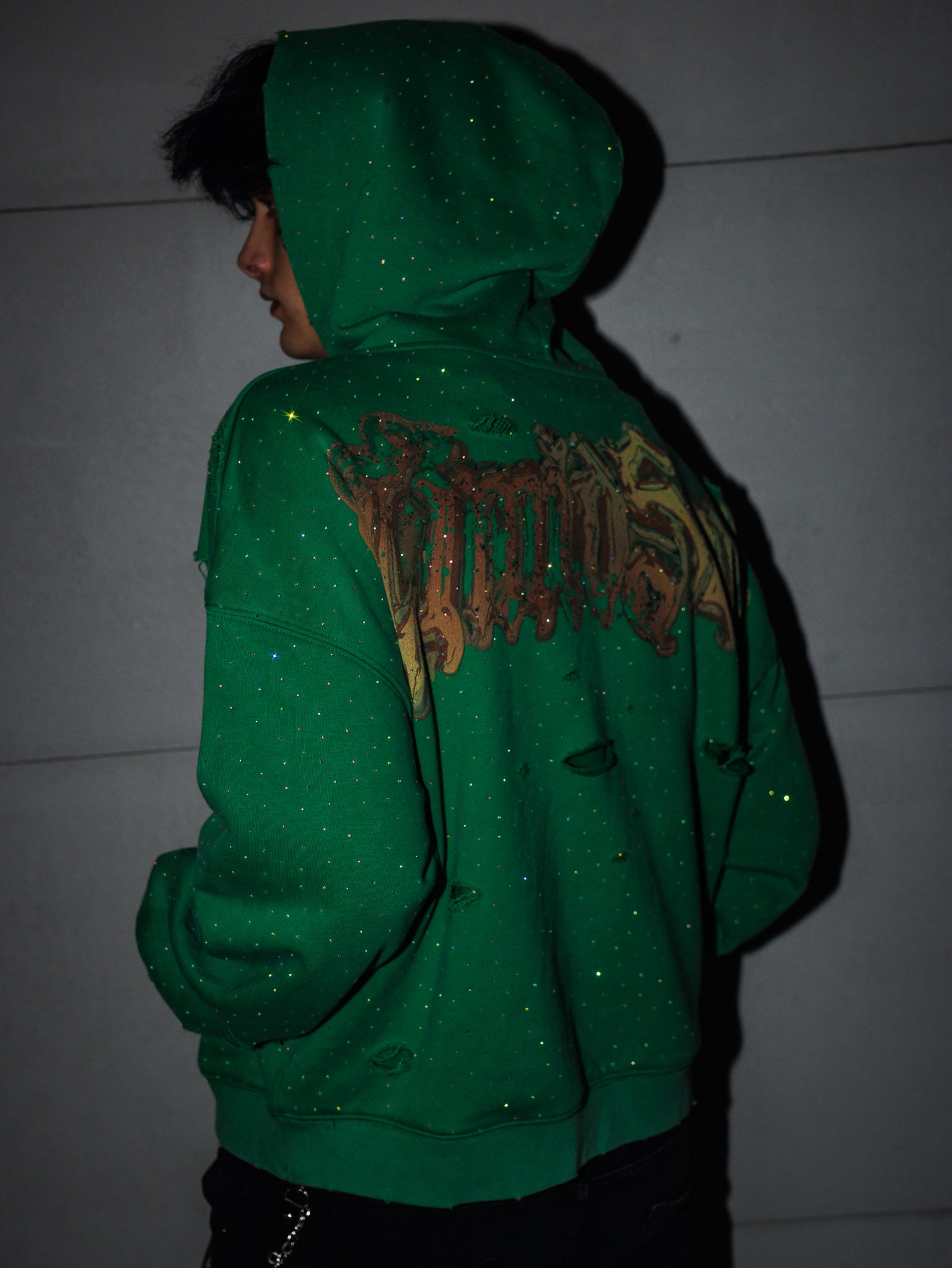 Person wearing a green hoodie with a graphic design on the back against a plain background