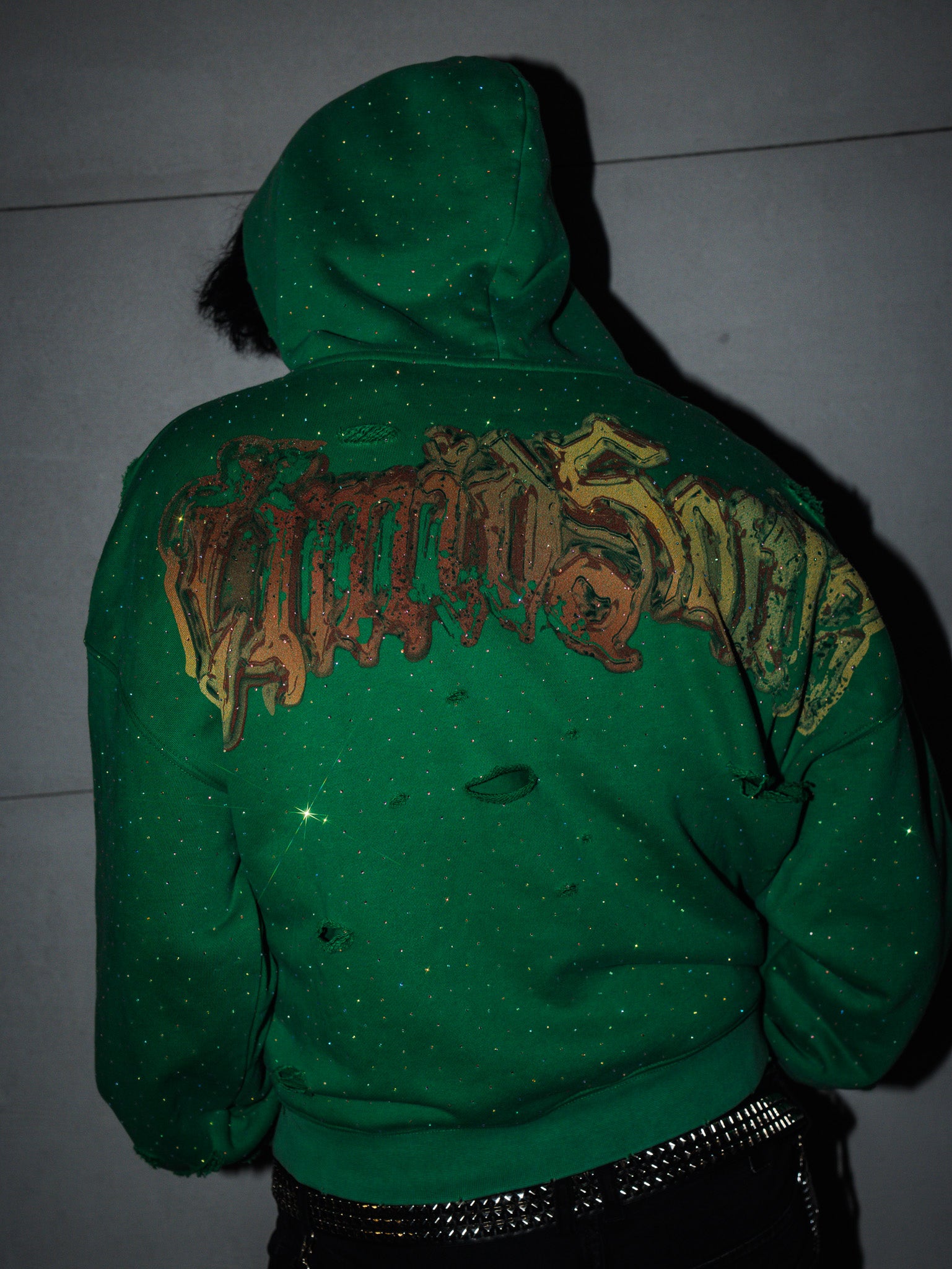 Green hoodie with graphic design on the back against a dark background