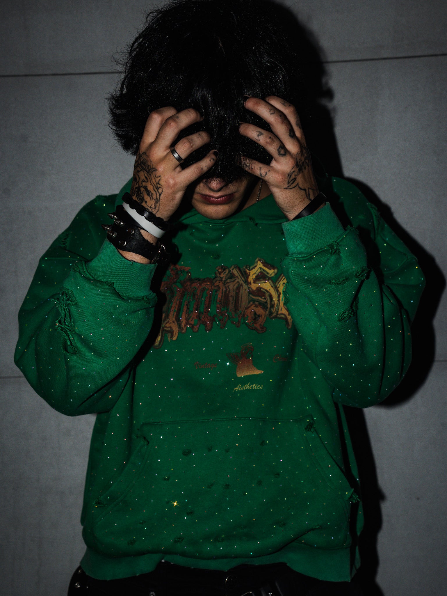 Person wearing a green hoodie with a logo, covering their face against a plain background