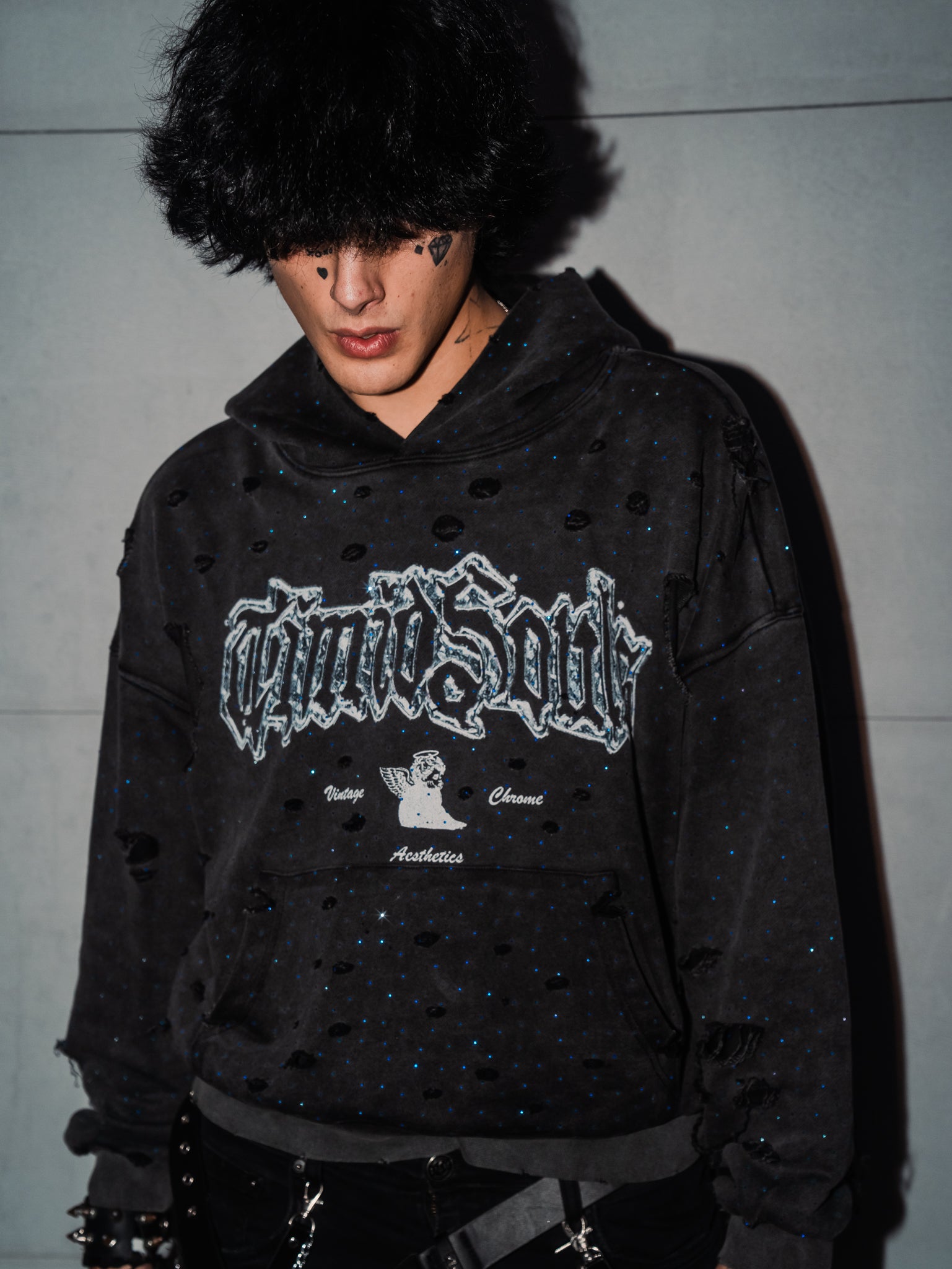 Person wearing a black distressed hoodie with a brand logo against a plain background