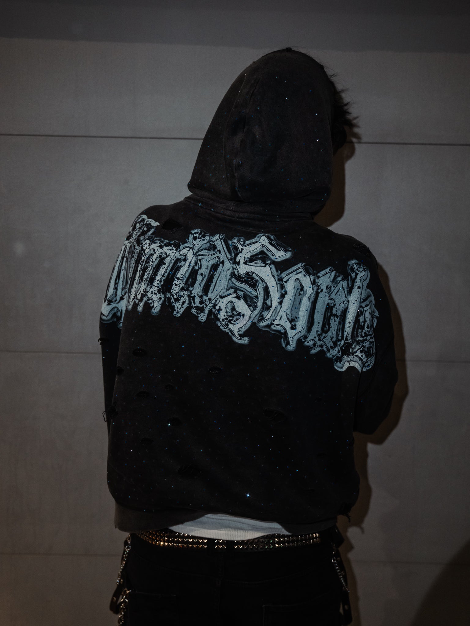 Person wearing a black hoodie with white text on the back against a plain background