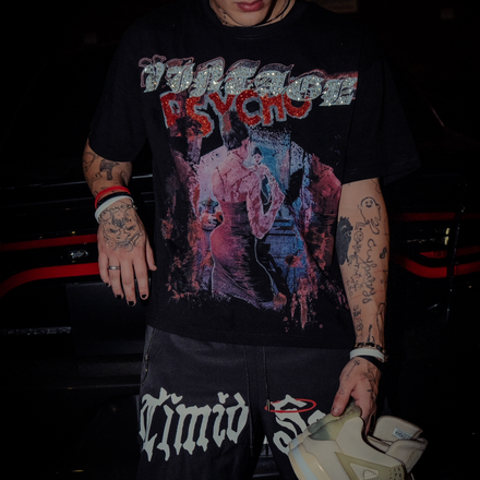 Person wearing a black t-shirt with graphic design and text, holding a white sneaker.