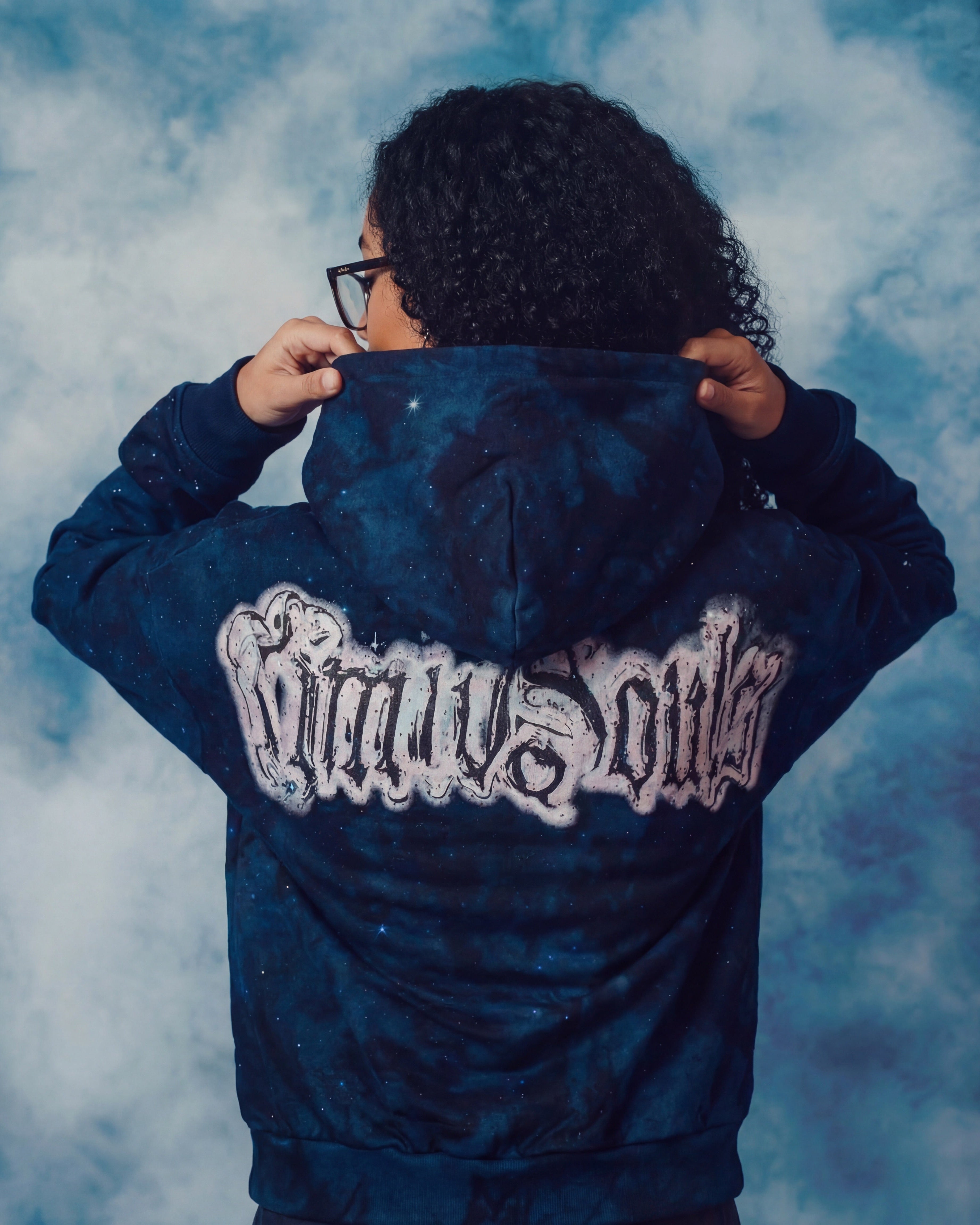 Person wearing a blue hoodie with text on the back against a cloudy sky background