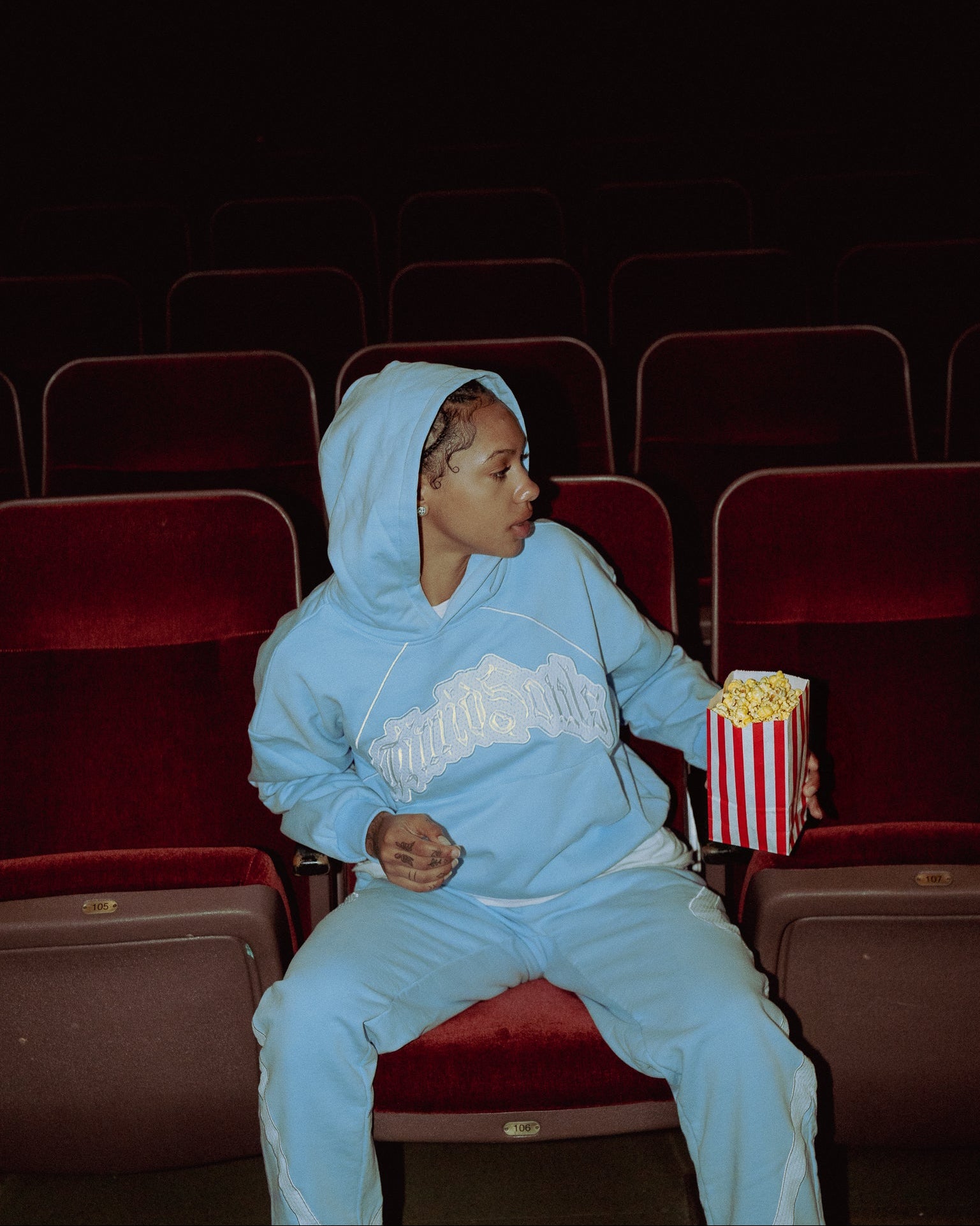 Person in a blue tracksuit sitting in an empty theater with popcorn.