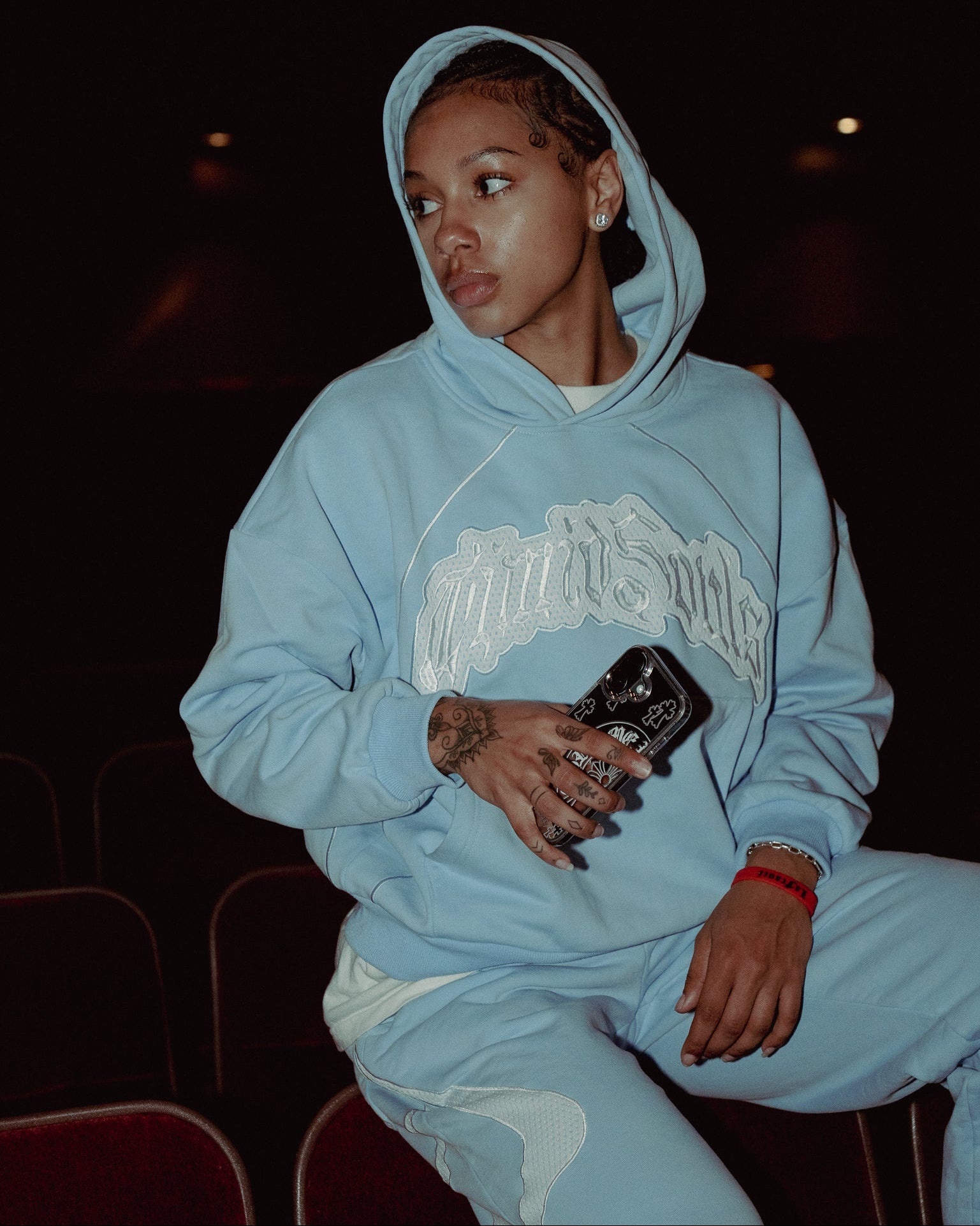 Person wearing a light blue hoodie with a logo, sitting in a dark room.