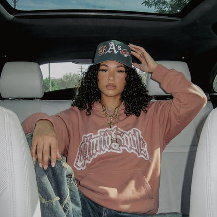 Person sitting in a car wearing a hoodie and cap, with a clear sky visible through the sunroof.
