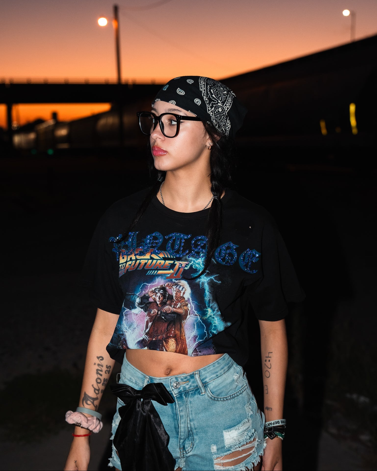 Person wearing a graphic t-shirt and denim shorts with a bandana at sunset.