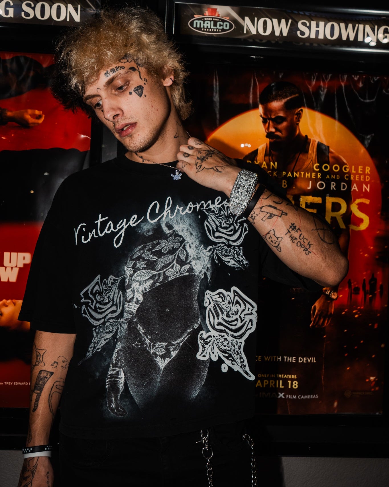 Person wearing a black t-shirt with graphic designs in front of movie theater screens.