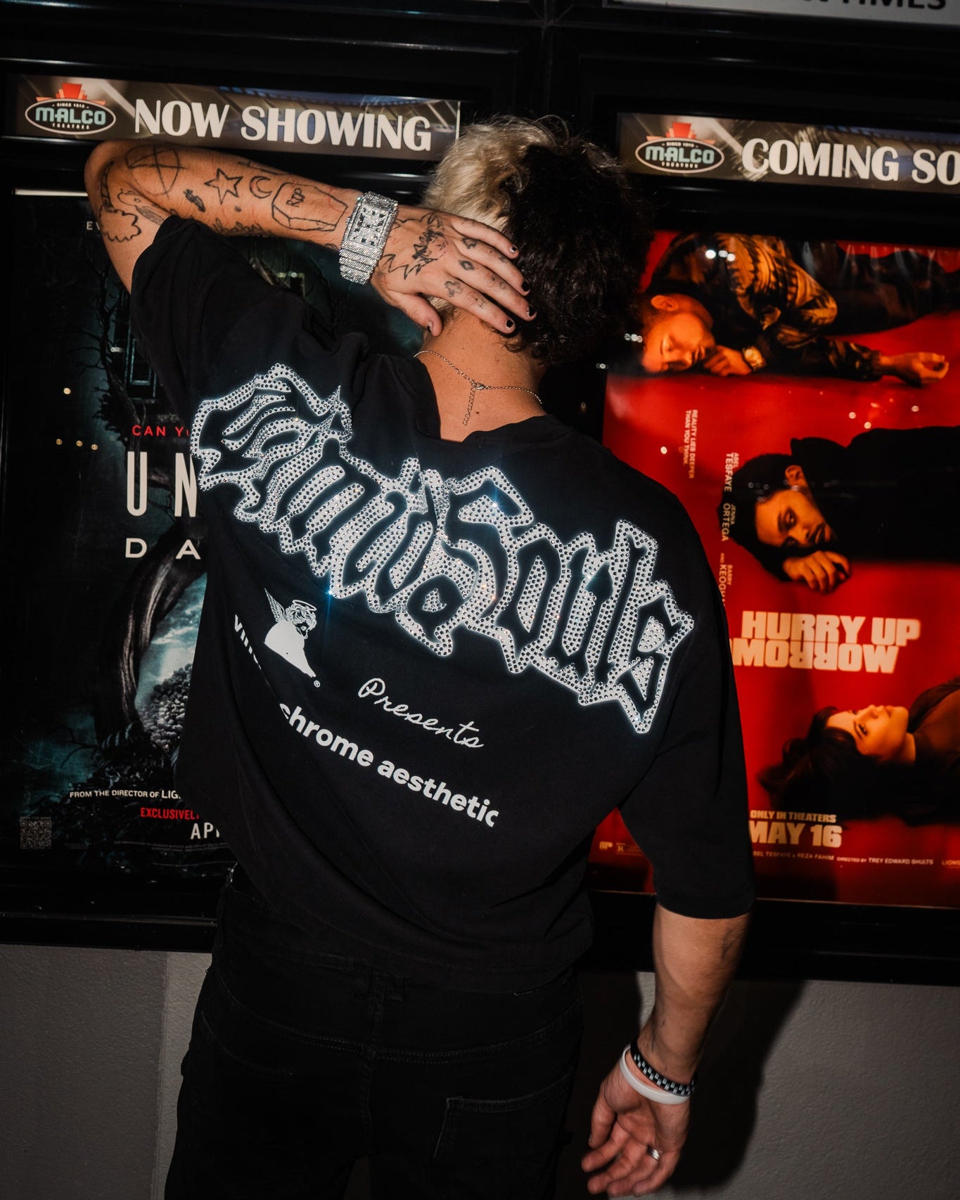 Person wearing a black t-shirt with white text in front of movie posters.