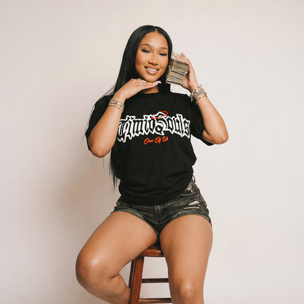 Woman sitting on a stool wearing a black t-shirt with text, holding a phone.