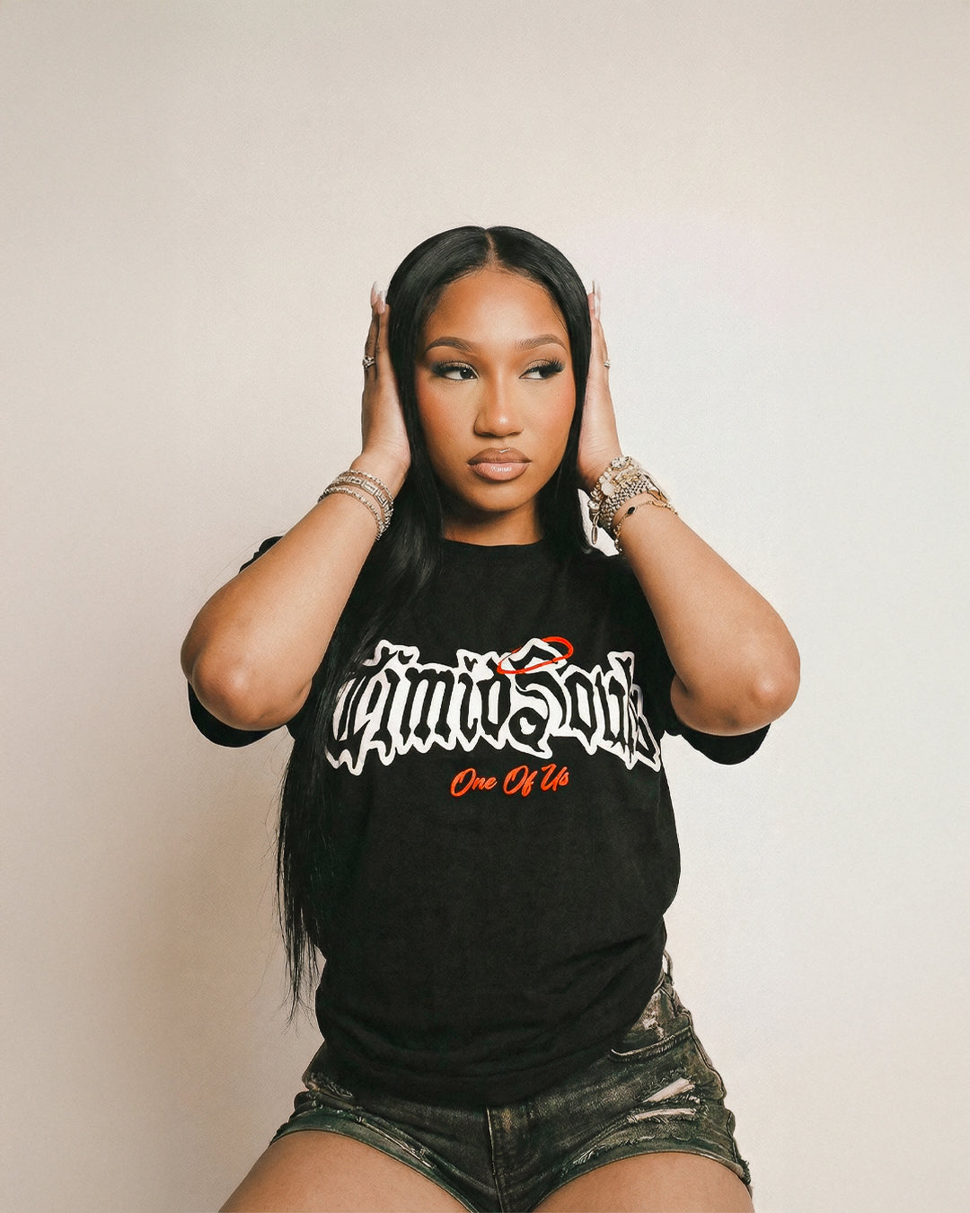 Woman wearing a black t-shirt with text, posing with hands on head against a plain background