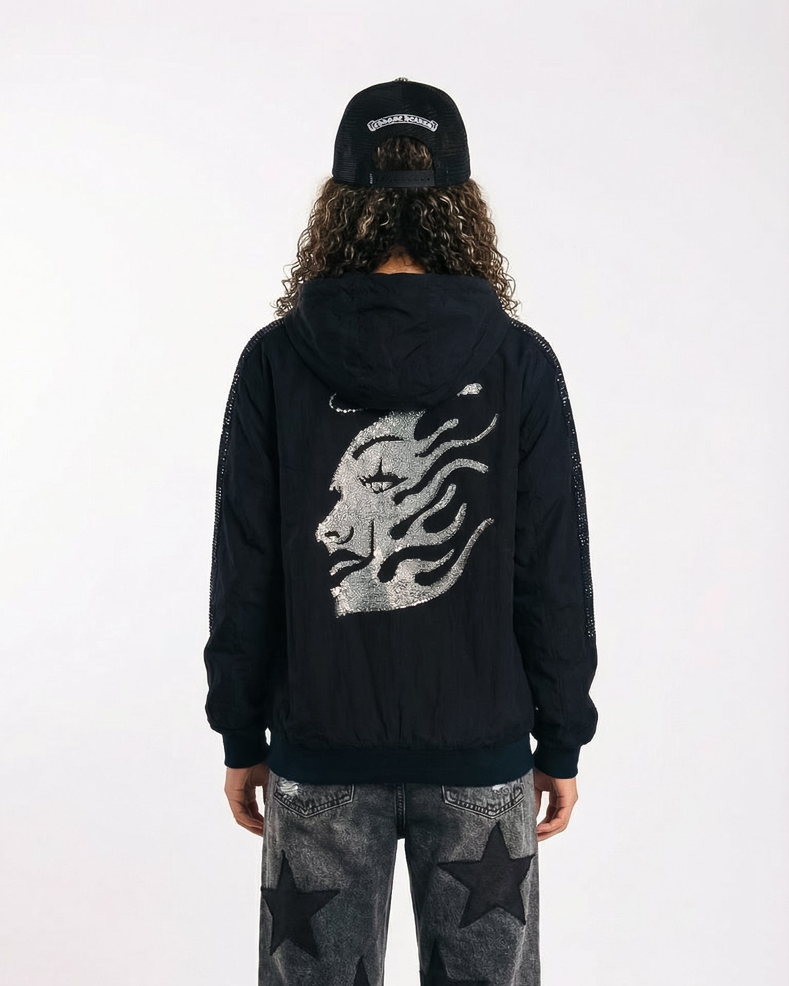 Person wearing a black hoodie with a graphic design on the back, standing against a white background.