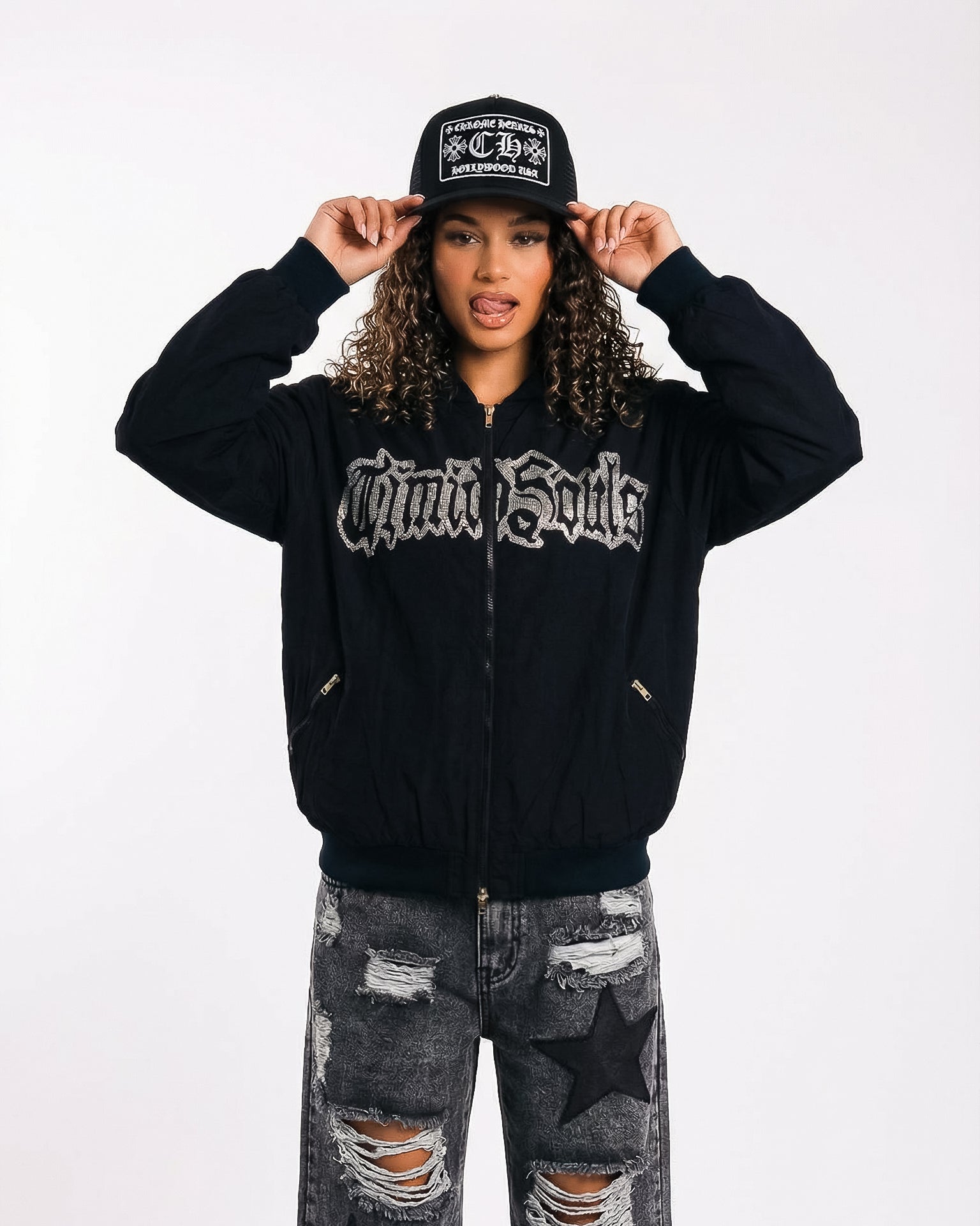 Person wearing a black hoodie with text, black cap, and ripped jeans on a white background