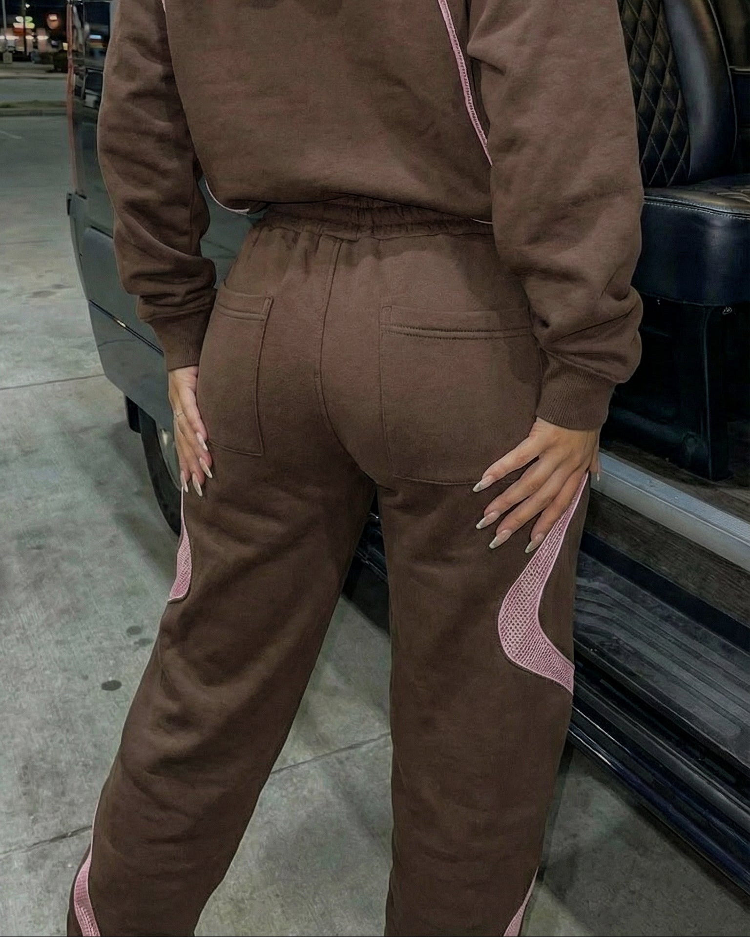 Person wearing a brown tracksuit with pink accents in a parking lot.