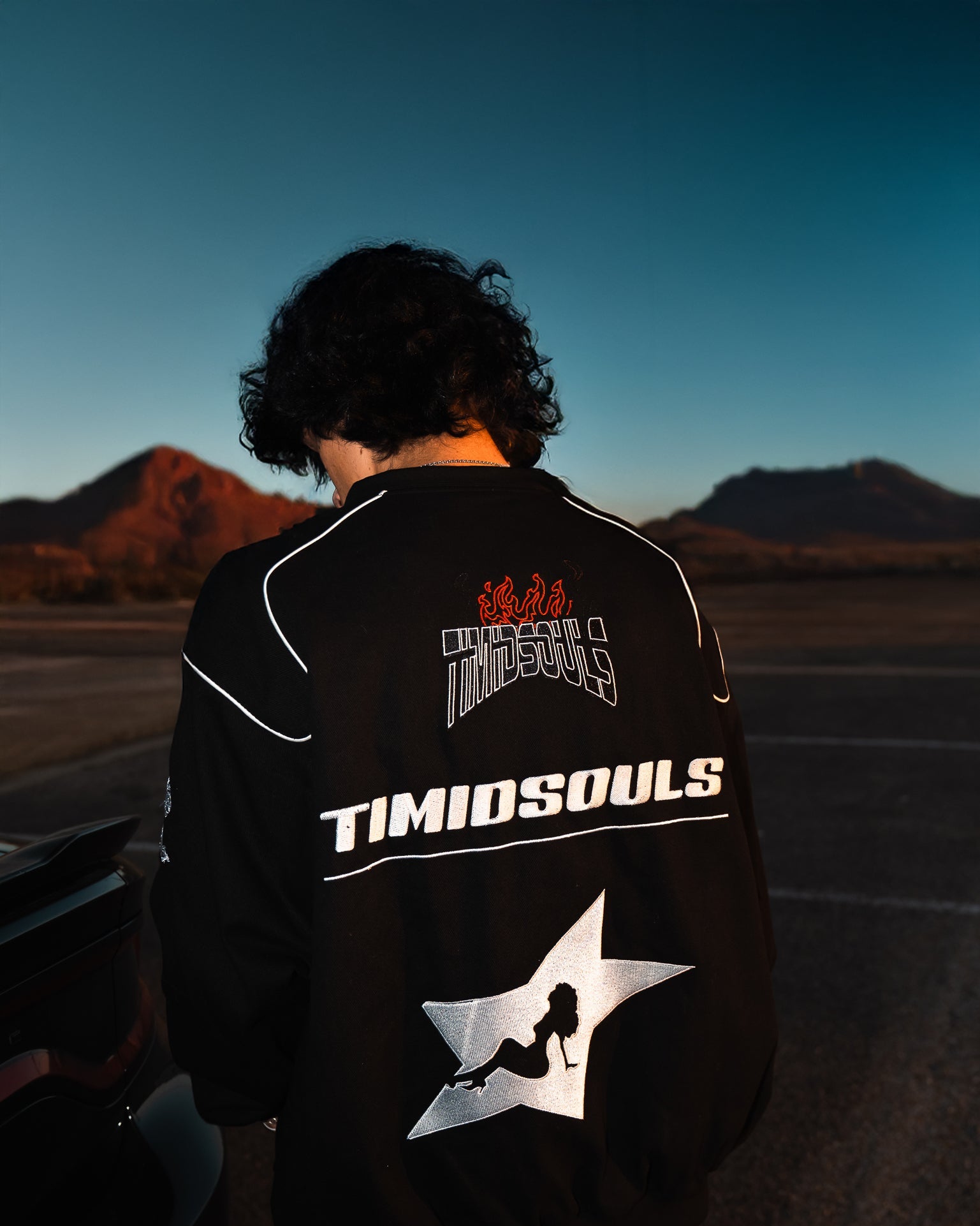 Person wearing a black jacket with 'TIMIDSOULS' branding in a desert setting