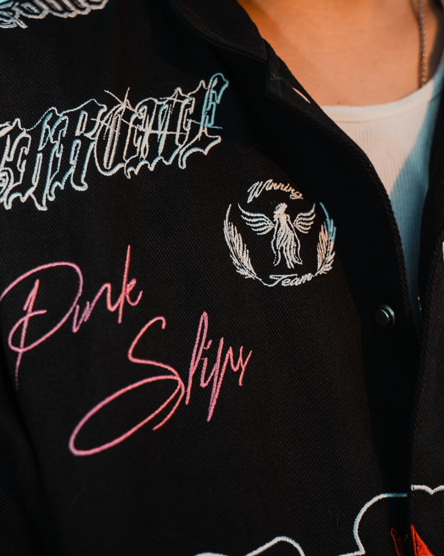 Black jacket with embroidered text and designs, including 'Pink Slips' in pink.