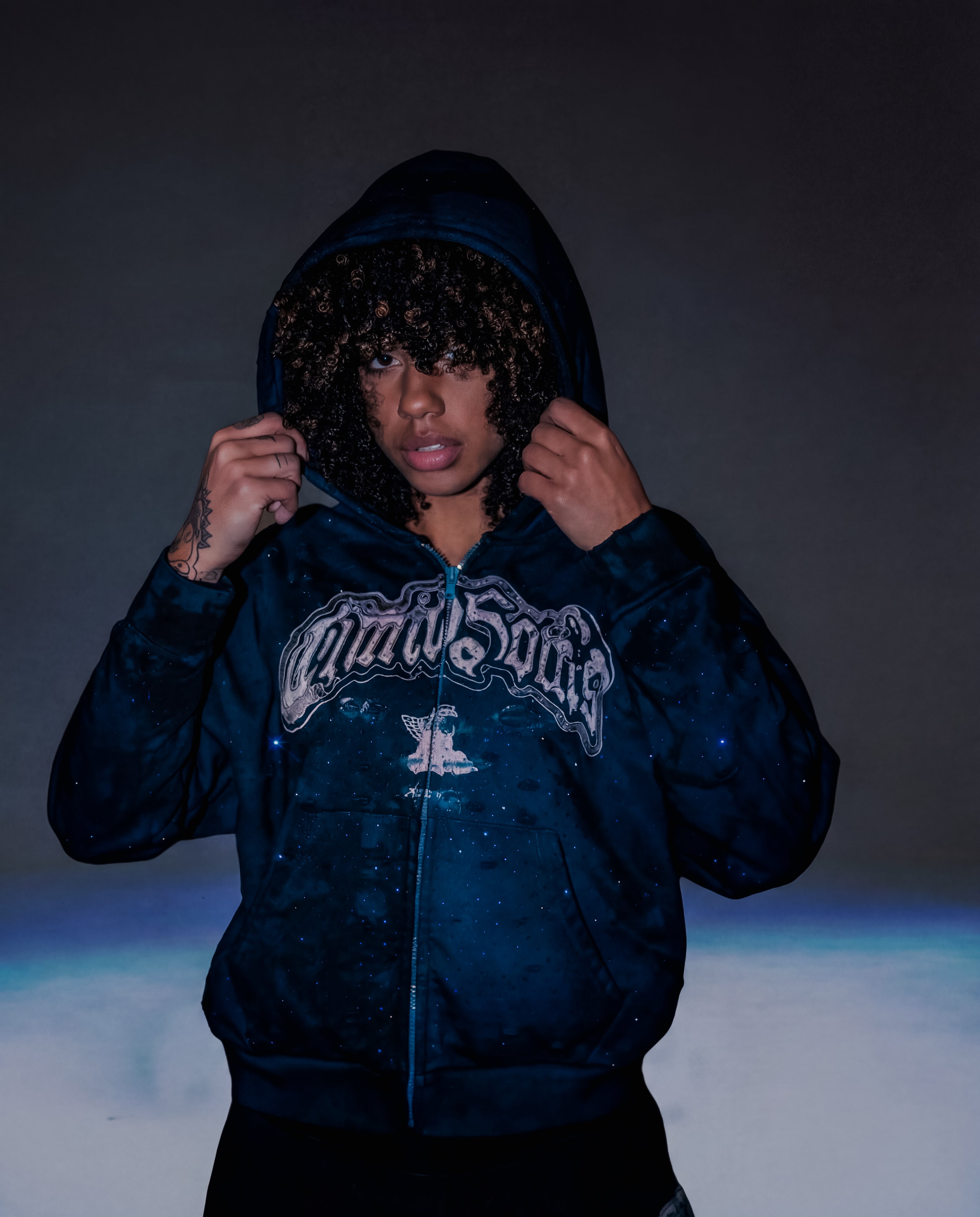 Person wearing a dark blue hoodie with a logo on a dark background