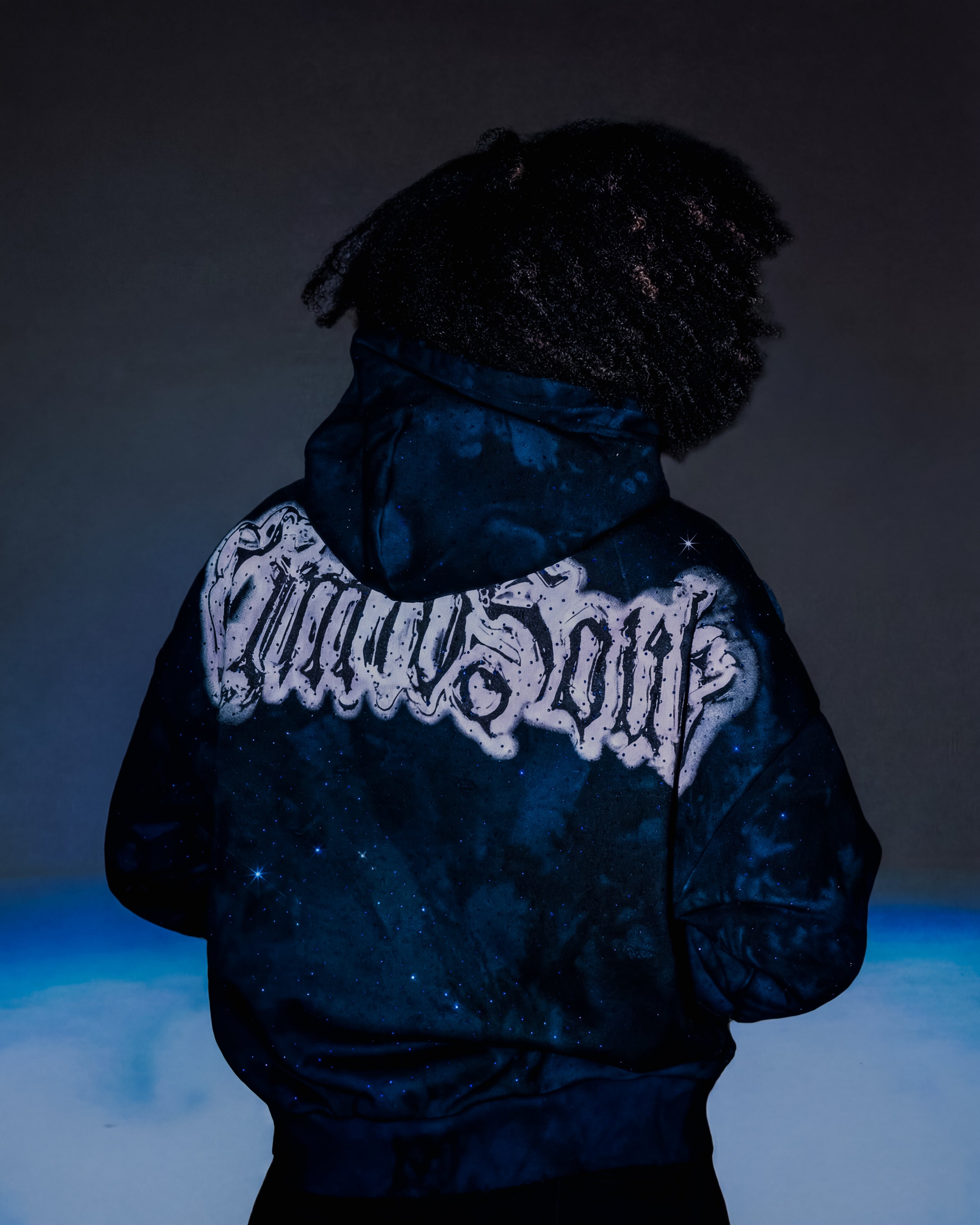 Person wearing a dark jacket with a visible brand logo on the back against a dark background.
