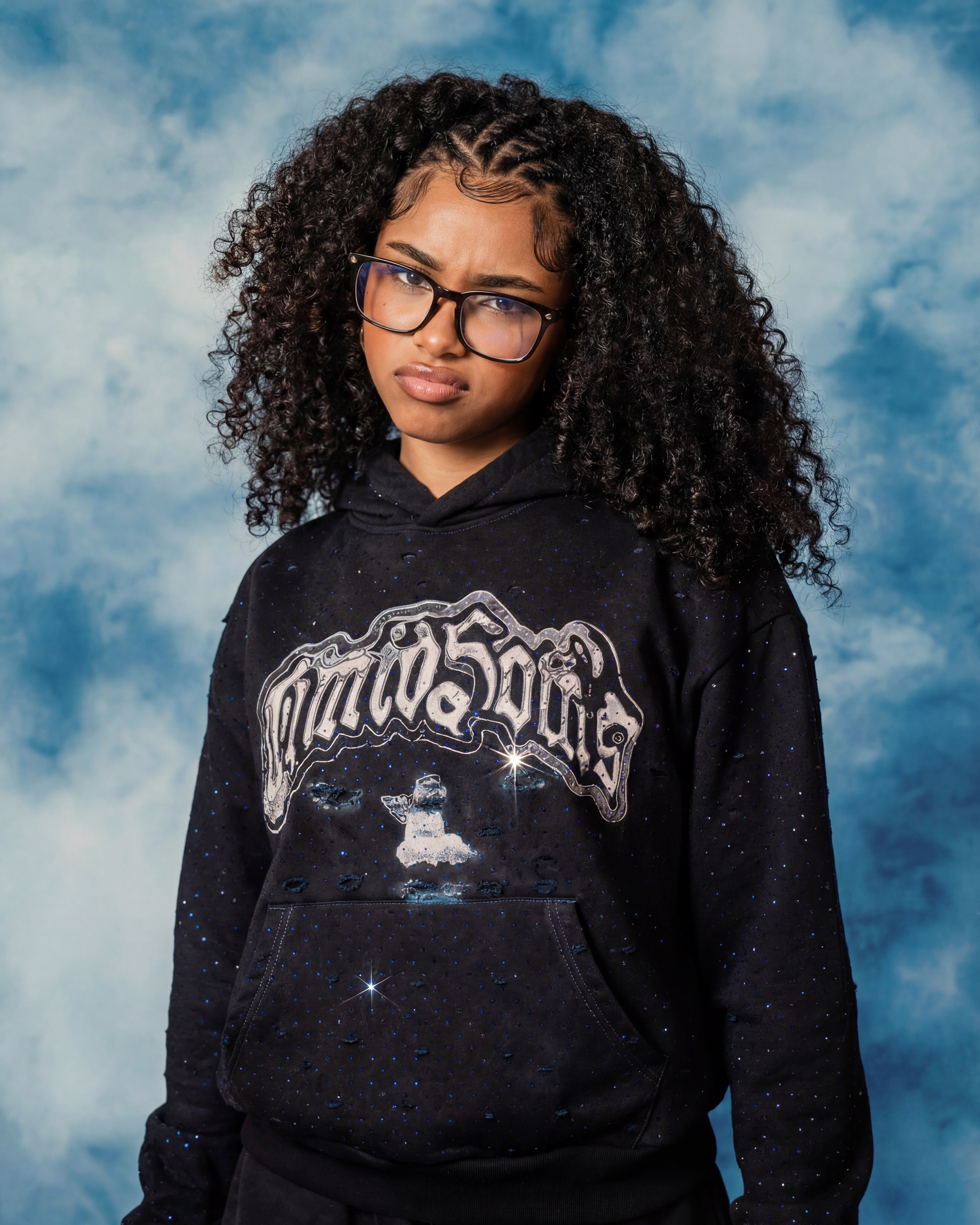 Person wearing a black hoodie with a logo against a blue sky background